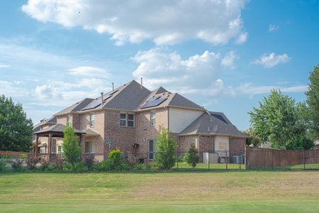 Two story suburban residential house with solar panel rooftop near rolling park side grassy lawn in Flower Mound, Texas, America. Clean and renewable energy alternative power supplyの写真素材