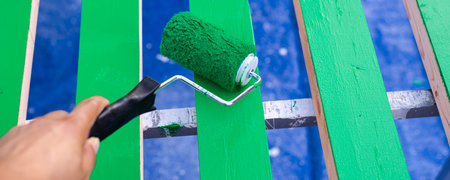 Panorama view Asian hand using 6 inches paint roller for second coat of latex paint smooth surface 2 by 4 wooden boards on sawhorse with blue tarp cover drops in Dallas, Texas, USA. Home remodel DIYの写真素材