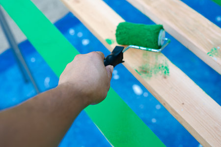 Hand using 6 inches paint roller for first coat of latex paint on 2 by 4 wooden boards on sawhorse with blue tarp cover paint drops outdoor in Dallas, Texas, USA. Home remodel renovation project DIYの写真素材