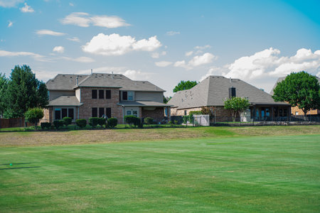 Large grassy and rolling lawn of suburban park next to upscale residential neighborhood row of two-story houses in Flower Mound, Texas, USA. New development homes with metal fence solar roof panelsの写真素材