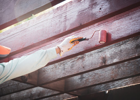 Asian man hand wears gloves using 4 inches roller stain pergola timber outdoor structure in redwood latex water based exterior stain color, home improvement DIY project, house renovation. Handymanの写真素材