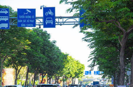 Traffic signs (translate security camera in use) above lush green tree-lined road on both sides...