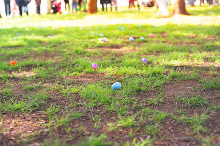 Colorful Easter egg on green grass meadow with blurry long line of diverse kids parents waiting for...