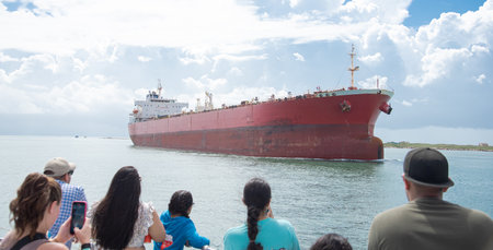 Panorama view diverse tourist sightseeing large crude oil tanker sailing thru Gulf Coast Laguna Madre in South Padre Island, South Texas, multiethnic group travelers from upper deck of tour boat. USAの写真素材