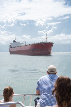 Diverse tourist sightseeing large crude oil tanker sailing thru Gulf Coast Laguna Madre in South Padre Island, South Texas, multiethnic group travelers from upper deck of tour boat cruise. USAの写真素材