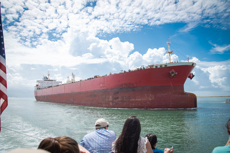American flag flying on tour boat with diverse tourist sightseeing large crude oil tanker sailing thru Gulf Coast Laguna Madre in South Padre Island, South Texas, multiethnic group travelers. USAの写真素材