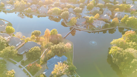 Water fountain and little dam between lakeside residential community in Coppell, suburbs Dallas, Texas colorful autumn leaves over row of two story large suburban houses swimming pools, aerial. USAの写真素材