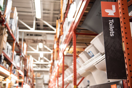 Looking up hardware store aisle full shelves of brand-new toilet bowls on display at home...