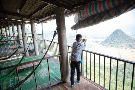 Hammocks, bamboo mat and safety balcony at Vietnamese mountainside restaurant with Asian toddler boy taking aerial landscape photo in Mai Chau, Hoa Binh, active kid in hoodie with digital camera. Asiaの写真素材