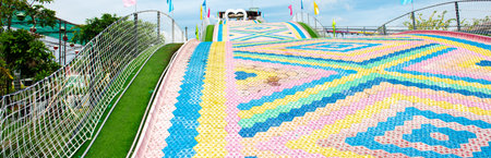 Panorama view rainbow dry slide made of plastic spread to artificial lawn on steel structure slope...