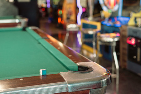 Cue chalk near chrome cast corners of classic pool tables with blurry colorful illuminated arcade...