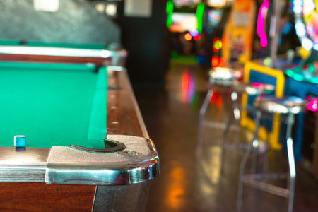Cue chalk near chrome cast corners of classic pool tables with blurry colorful illuminated arcade...