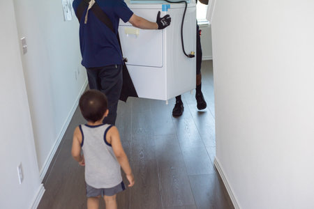 Asian toddler boy following professional mover uses lifting straps to distribute weight ergonomically when carry large dryer appliance at new home in Princeton, Texas, home delivery service. USAの写真素材