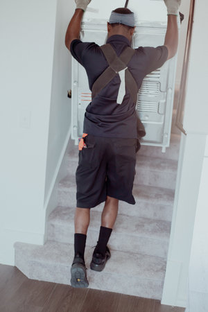 Rear view professional mover uses lifting straps to distribute weight ergonomically when carry large dryer household appliance up carpeted staircase at new home in Princeton, Texas, safe moving. USAの写真素材