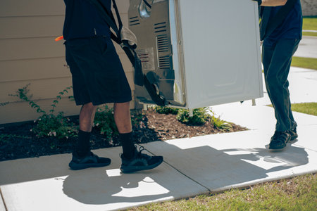 Professional mover uses lifting straps to carry large household appliance along sidewalk new house entrance, landscaping, and siding, suitable for home services, appliance delivery, moving themes. USAの写真素材