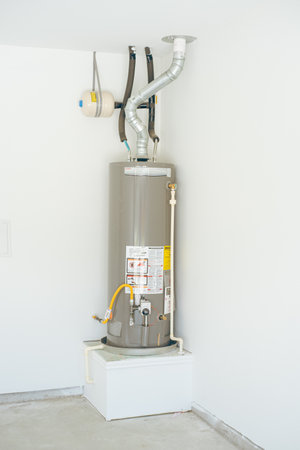 Corner pedestal stand for gas water heater in garage with expansion tank, insulated pipes, vent system, yellow gas line, shut-off and pressure relief valves for Texas code-compliant installation. USAの写真素材
