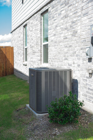 Outdoor HVAC unit and wall mounted electrical boxes installed alongside modern brick home, clean siding and windows, green grass landscaping shrub, privacy fence, disconnect switch, utility meter. USAの写真素材