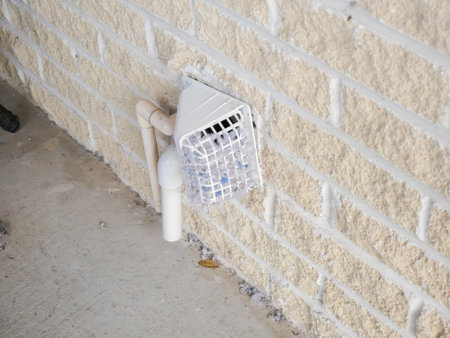 Side view heavily clogged lint dryer vent cover on brick wall, blocking airflow, posing fire hazard. Visible adjacent PVC pipes, buildup highlights poor ventilation, maintenance cleaning needed. USAの写真素材