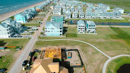 Aerial view residential construction near ocean shoreline with framing work, roofing, heavy equipment, and sandy terrain, vacant land, energy and scale of active development in Galveston, Texas. USAの写真素材