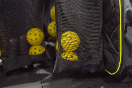 Bright yellow pickleball balls and paddles in black mesh bags on display at sport retailer in...