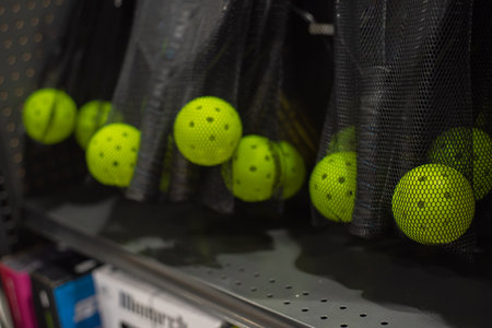Functional, space-efficient sports equipment management, retail environments tidy storage solutions pickleball paddles and yellow balls stored in mesh bags hanging from perforated metal shelving. USAの写真素材
