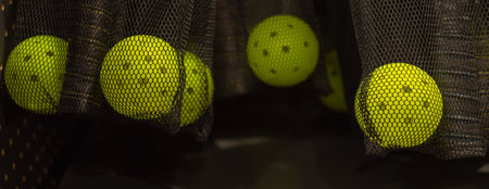 Panorama view yellow perforated pickleball balls and matching paddles stored together in breathable...