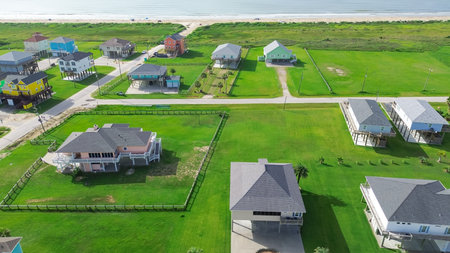 Long stretch of oceanfront residential development with low-density colorful raised beach houses, set apart by spacious grassy backyards, vacant land near sandy shoreline in Port Bolivar, Texas. USAの写真素材