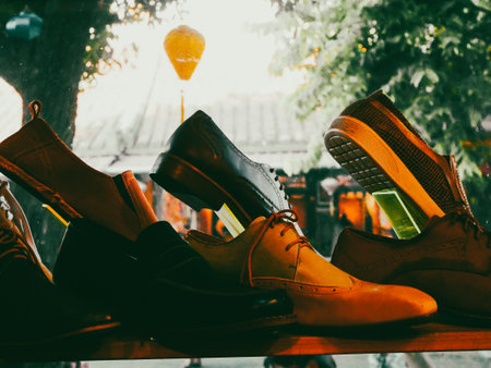 Handmade women leather sandals strappy, open-toe, and slingback on display in Danang, blurred view of tourists, old tile-roofed houses, leafy street scene evoking charm and artisanal heritage. Vietnamの写真素材