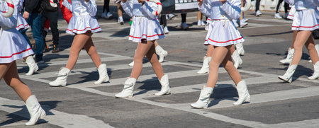 Panorama view young parade performers march in formation wearing white cowboy boots, brown knee-high socks, flared skirts with red trim. Attire adds texture and rhythm festive street choreography. USAの写真素材