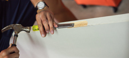 Panorama view relaxed seated craftsman carefully guides yellow-handled chisel along the edge of door...