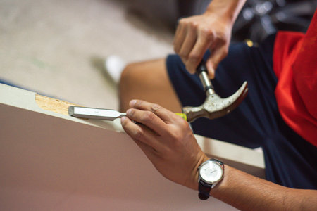 Selective focus Asian craftsman refining a white door slab mortise hinge with a chisel and claw hammer, wearing a traditional wristwatch, set against a blurred garage backdrop workshop element. USAの写真素材
