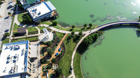 Lakeside restaurant patios with umbrellas, circular pond, paved trails, and pedestrian bridge near...