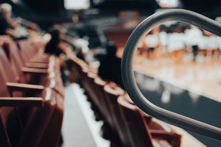 Angled view of empty red stadium seats section with metal safety rails. Blurry players, audience members in background suggest relaxed basketball event in clean venue at college in Dallas, Texas. USAの写真素材