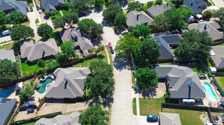 Residential street close-up in North Richland Hills featuring upscale two-story homes with backyard pools, mature shade trees, and spacious lots arranged along curved, well-maintained roads, TX. USAの写真素材
