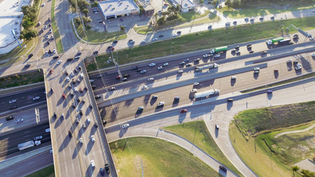 Modern infrastructure transportation system with overpass structure, multilane highway intersection tollway, busy traffic flow, flat-roof buildings industrial HVAC units, service access roads. USAの写真素材