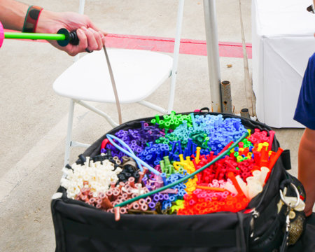 Artist using hand pump to inflate balloon with children hands surround black bag filled with organized tubes, capturing a busy moment at twisting station family friendly event.の写真素材