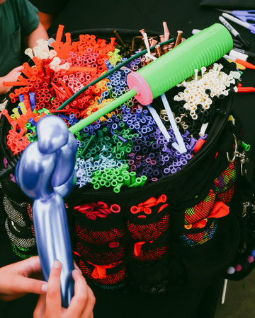 Kids hand holding shiny blue twisted balloon near green-pink hand pump on top of black bag kit displays long balloons sorted by color. public entertainment event, craft activity in Dallas, Texas. USAの写真素材