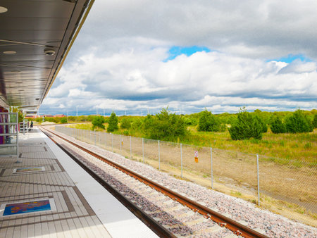 Passenger waiting at rail station near DFW Airport multiple tracks diverging. ADA-accessible platform includes security camera, accessibility signs, lush vegetation and safety railings in view. USAの写真素材