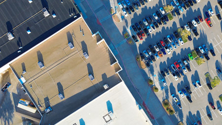 Angled view across frame of large retail strip with flat roof HVAC units and facade-facing parking. Gas and electric vehicles, ADA zones, landscaped medians show suburban planning efficiency, TX. USAの写真素材