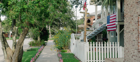 Panorama view directional signpost next to white picket fence front yard house features porch American flag, wooden chairs, brick siding home in background, patriotic scene in Galveston, Texas. USAの写真素材