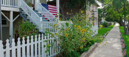 Panorama view of a two-story light green house features a porch with string lights, ceiling fan, American and Texas flags, decorative accents, festive charm, and patriotic decor in Galveston, Texas.の写真素材