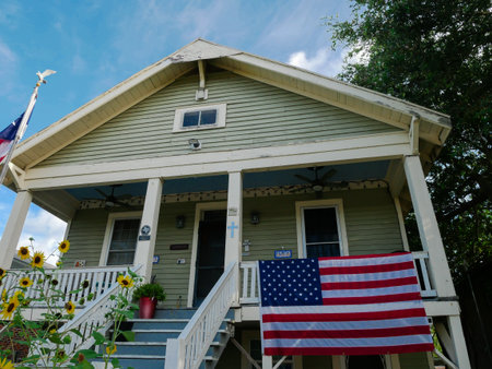 Large American flat at two-story light green house features porch string lights, ceiling fan, USA and Texas flags, decorative accents, blending elevation and festive charm in Galveston, Texas. USAの写真素材