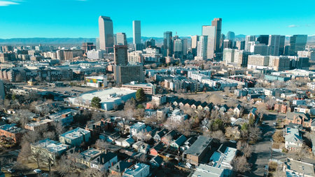 Historic core neighborhoods west of Cheesman Park toward glass towers, downtown skylines, mountain range near Franklin St. Mixed rooflines, muted foliage, varied exterior tones in Denver, CO. USA