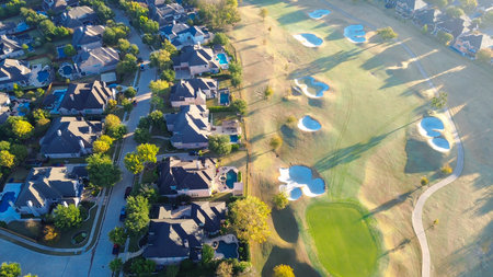 Aerial view clustered blocks of upscale large mansion homes beside Lantana Golf Club sit near greens and sculpted sand pockets. Low sun angles emphasize roof textures, tree shadows in Texas. USAの写真素材