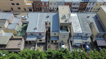 Vertical axis neighborhood run along S 10th St shows continuous rowhome blocks framed by cross streets and green parkland. Flat roofs, masonry tones, soft atmospheric diffusion, Philadelphia, PA. USA