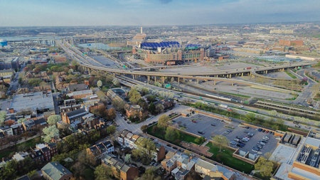 Stadium interchange sweep system near Russell St displays looping ramps, adjacent neighborhoods stretching toward Patapsco shoreline. Mixed rooflines define urban infrastructure Baltimore, MD. USA
