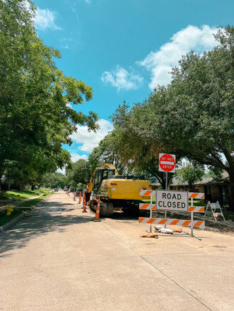 Full closure barricade presents blocked lane with cones, striped panels, restriction signs before parked excavator. Clean structural spacing, roadway edges, construction scene in Coppell, TX. USA
