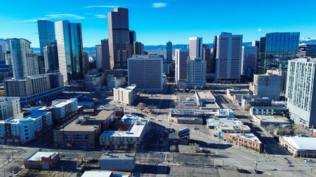 Dense clusters of office towers contrast with quiet, treelined streets near urban periphery. Intense solar reflections dance across industrialstyle building envelopes in cityscape of Denver, CO. USA