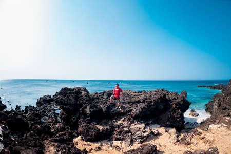 A young girl in a red swimsuit walks along the coast.の写真素材