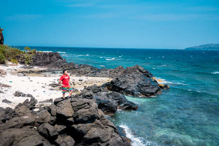A woman in a red dress is standing on a rock and looking at the sea